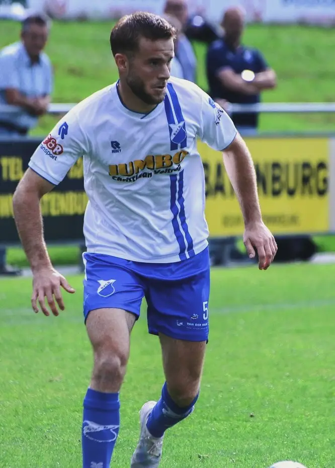 Een speler van BVCB in het blauw-witte shirt loopt geconcentreerd over het veld, de bal net voor zijn voeten.